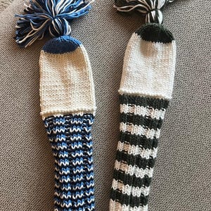 May include: Two knitted golf club covers with pom-poms. One is white, blue, and navy, the other is white and green striped. The text "Knitting Pattern" is at the top of the image.