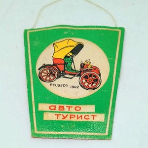 May include: A vintage green and white car-themed souvenir with a string for hanging. The design features a red and yellow antique car illustration within a white circle, with the text "PEUGEOT 1902" and Cyrillic text "ABTO TУРИСТ".