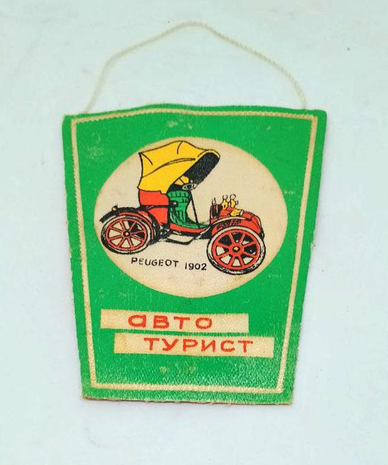 May include: A vintage green and white car-themed souvenir with a string for hanging. The design features a red and yellow antique car illustration within a white circle, with the text "PEUGEOT 1902" and Cyrillic text "ABTO TУРИСТ".