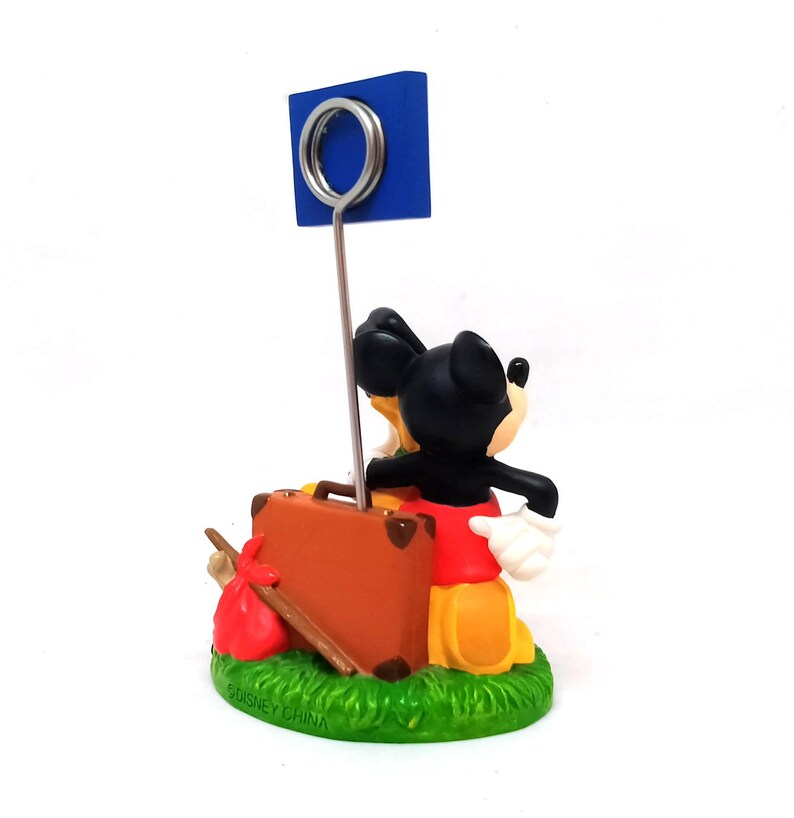 May include: A Mickey Mouse figurine with a blue sign holder. Mickey is dressed in his classic red shorts, yellow shoes, and white gloves, carrying a brown suitcase and a red sack. The base is green with the text "&copy; DISNEY CHINA".
