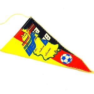 May include: A triangular pennant featuring a map of Germany in yellow, red, and black. The design includes the text 'VB 78', city names like Köln, Frankfurt, and Stuttgart, and a graphic of a soccer ball. A yellow cord is attached for hanging.
