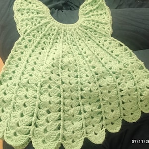 May include: A light mint green crochet garment featuring a circular yoke and a flared, fan-like stitch pattern throughout the body. The piece has a scalloped hemline and a round neckline, constructed with a repeating textured yarn design.