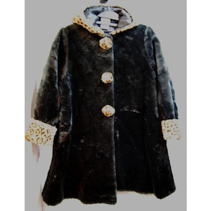 May include: A black faux fur coat with a hood and three large decorative buttons. The hood and cuffs feature a tan and brown animal print. The coat is hanging on a white hanger.