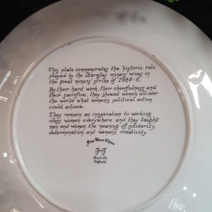 May include: A white Fine Bone China plate with black text commemorating the Barnsley miners' wives' role in the 1984-5 miners' strike. The plate's text highlights their hard work, cheerfulness, and sacrifice.