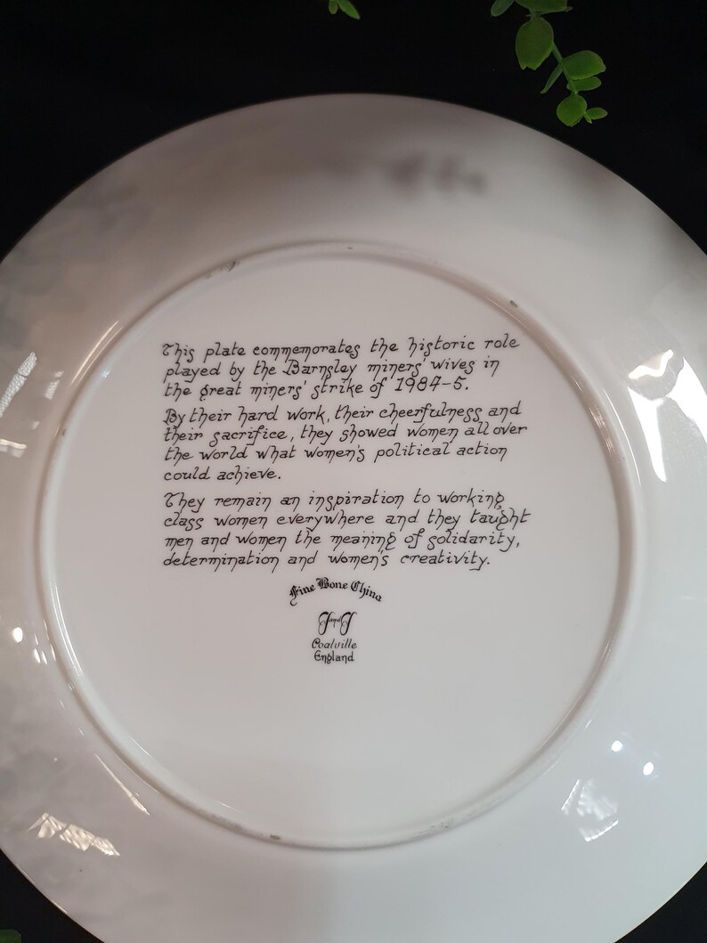 May include: A white Fine Bone China plate with black text commemorating the Barnsley miners' wives' role in the 1984-5 miners' strike. The plate's text highlights their hard work, cheerfulness, and sacrifice.