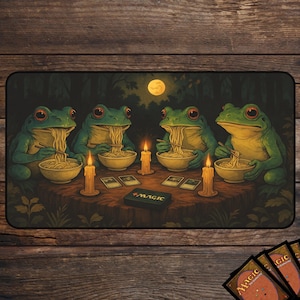 Puede incluir: Alfombrilla de juego con cuatro ranas verdes de ojos rojos, comiendo fideos alrededor de una mesa, iluminada por velas y una luna llena. Hay una caja con la palabra "MAGIC", junto con varias cartas de Magic: The Gathering.