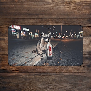 May include: A rectangular mousepad featuring a raccoon wearing sunglasses, holding a Diet Coke can with a straw, and sitting on a curb. The background shows a city street at night with a bar and the text "BAR 24HR".
