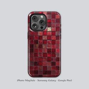 Puede incluir: Una funda de teléfono con un diseño de mosaico en tonos rojos. La funda tiene un acabado brillante y un patrón cuadrado. Las lentes de la cámara son visibles en la parte superior. El texto en la parte inferior dice "iPhone MagSafe • Samsung Galaxy • Google Pixel".
