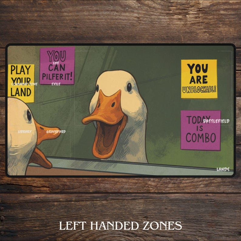 K&ouml;nnte beinhalten: Rechteckige Spielmatte mit einer Cartoon-Enten-Illustration und verschiedenen Textelementen. Der Text enth&auml;lt S&auml;tze wie "PLAY YOUR LAND", "YOU CAN PILFER IT!" und "YOU ARE UNBLOCKABLE". Die W&ouml;rter "LIBRARY" und "GRAVEYARD" sind ebenfalls sichtbar.