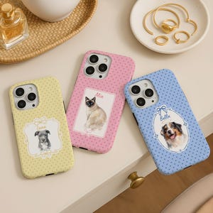 May include: Three phone cases with pet portraits. One is yellow with a dog named Luna, another is pink with a cat named Mia, and the third is blue with a dog named Bella. Each case has a polka dot pattern.