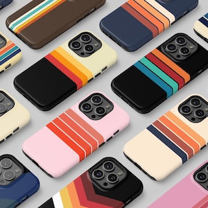 以下が含まれることがあります： レトロストライプデザインのスマートフォンケースのコレクション。クリーム、黒、ピンク、青など、さまざまな色があり、オレンジ、黄色、ティール色の水平ストライプがあります。スマートフォンに合うように設計されています。