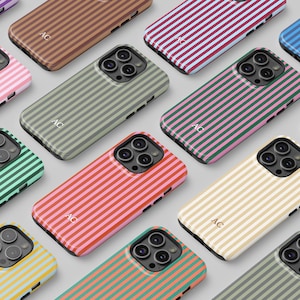 May include: A collection of colorful phone cases with vertical striped patterns. Cases are in various colors including pink, green, yellow, and blue. Each case has a camera cutout and the initials "AC" printed on the case.