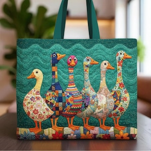 Può includere: Una borsa tote verde acqua con un design trapuntato di cinque oche colorate. Ogni oca ha un motivo unico di fiori, patchwork e forme geometriche. La borsa ha manici verde acqua e uno sfondo verde acqua con un motivo ondulato.