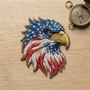 May include: Embroidered patch featuring an American bald eagle head. The eagle's head is depicted with blue, white, and red colors, representing the American flag. The patch is detailed with intricate stitching and a gold beak.