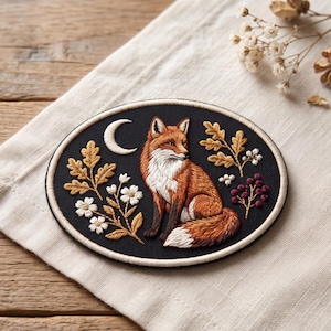 May include: An oval embroidered patch on a black fabric background featuring a red fox sitting centrally. The design includes a white crescent moon, golden oak leaves, white flowers, and small dark red berries, all bordered by a cream-colored edge.