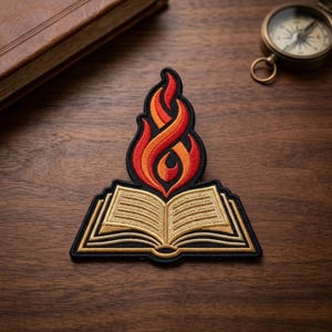 May include: An embroidered patch featuring an open book with cream-colored pages and black outlines, topped with a stylized flame design in vibrant shades of red and orange, all bordered by a thick black thread edge on a dark fabric base.