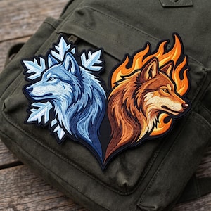 May include: An embroidered patch featuring two wolf heads facing away from each other. The left wolf is blue and surrounded by a white snowflake design, while the right wolf is orange and brown, framed by stylized orange and yellow flames.