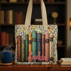 May include: A tote bag with a floral pattern and cream-colored handles. The bag features a design of vintage book spines. The name "Sophia" is written in a cursive font on the bag. The floral pattern includes yellow, orange, and purple flowers.