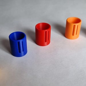 May include: Five brightly coloured, cylindrical objects with vertical slots. The objects are arranged in a row and are yellow, blue, red, orange, and light blue. The objects are made of a solid material and have a smooth finish.