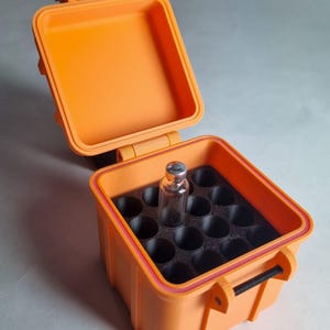 May include: An open orange plastic case with a black foam insert containing circular compartments. A small glass bottle with a silver cap sits in one compartment. The case has a hinged lid and a black handle.