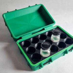 May include: Open green plastic case with a black interior and circular compartments. Two small glass bottles with black lids are inside. The case is open, revealing the interior and the bottles. The case has a handle and latches.