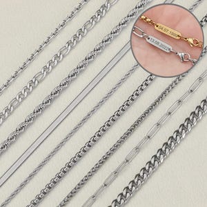 May include: An assortment of silver-colored chain necklaces in various styles, including figaro, rope, and herringbone. A close-up shows a gold-colored chain with engraved dates. The chains are displayed on a light-colored surface.