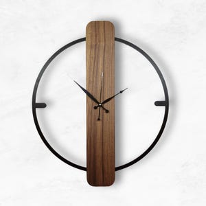 Könnte beinhalten: Eine moderne Wanduhr mit minimalistischem Design. Sie verfügt über einen Mittelteil aus dunklem Holzmaserung und einen kreisförmigen Rahmen aus schwarzem Metall. Die Zeiger sind schwarz, und die Gesamtästhetik ist sauber und modern.