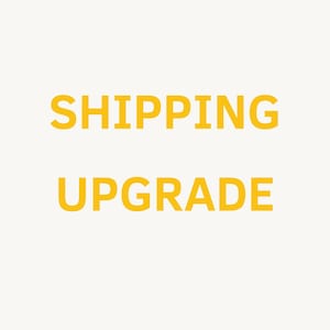 May include: A graphic design featuring the text SHIPPING UPGRADE in bold, yellow, sans-serif capital letters centered on a plain, off-white background. The text is arranged in two lines with the word SHIPPING on top and UPGRADE below it.