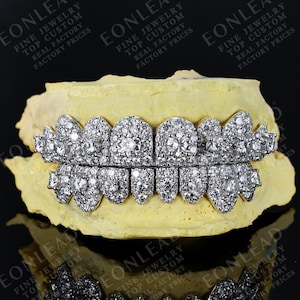 May include: A set of custom diamond grillz, showcasing a dazzling display of white gemstones. The grillz are set on a yellow dental mold, with the text "EONLEAD FINE JEWELRY TOP CUSTOM REAL FACTORY PRICES" visible in the background.