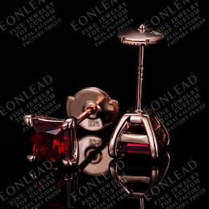 Op de afbeelding: Roségouden oorstekers met vierkante, dieprode edelstenen. De oorbellen hebben een vier-klauwzetting en een vlindersluiting. De afbeelding bevat de tekst "EONLEAD FINE JEWELRY TOP CUSTOM REAL FACTORY FACTORY PRICES".