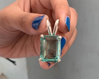 May include: A rectangular, light teal pendant with a silver bail. The gemstone is faceted, and the pendant is held up by a silver bail. The pendant is held up by a silver bail.