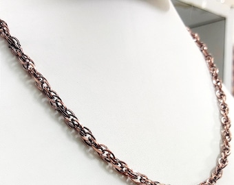 May include: A copper-colored chain necklace with a rope-like design. The necklace is displayed on a white mannequin, showcasing its intricate links and metallic sheen. The chain is a classic jewelry piece.