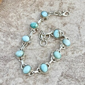 Peut inclure: Un bracelet en argent orné de pierres précieuses ovales bleu clair. Le bracelet présente un design en forme de chaîne, chaque pierre étant sertie dans une lunette en argent. Le fermoir est de type homard. Les pierres sont bleu clair et turquoise.