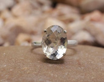 Könnte beinhalten: Ein Silberring mit einem großen, oval geschliffenen, hellgrünen Edelstein. Der facettierte Edelstein fängt das Licht ein und erzeugt einen funkelnden Effekt. Der Ring ist auf einem schlichten, polierten Silberband gefasst.