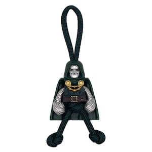 Peut inclure: Un porte-clés représentant le personnage de Dr. Doom, de couleur vert foncé. Le porte-clés présente un masque argenté, une cape vert foncé et des bras argentés. La poitrine du personnage est ornée d'une ceinture et d'éléments dorés. Le porte-clés est fait d'une corde vert foncé.