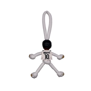 Może przedstawiać: Biały ceramiczny kubek z czarnym uchwytem i napisem "But First, Coffee" czarną, odręczną czcionką. Kubek stoi na białej powierzchni.