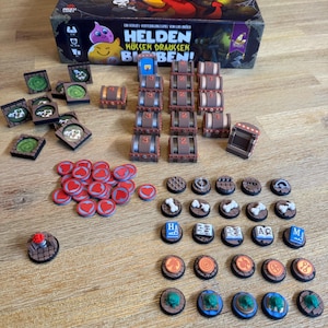 Könnte beinhalten: Ein Brettspiel-Set mit einer Box mit Cartoon-Charakteren und dem Text "HELDEN MÜSSEN DRAUSSEN BLEIBEN!". Das Set enthält verschiedene Spielsteine wie Truhen, Spielmarken und runde Plättchen.
