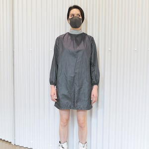 May include: A person wearing a dark gray, long-sleeved dress with a gray turtleneck and a matching face mask. The person is also wearing white boots with black soles.