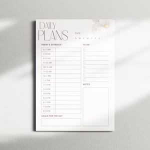 May include: A white daily planner with the words "DAILY PLANS" at the top. The planner includes sections for the schedule, to-do list, notes, and goals for the day. A floral design is in the upper right corner.