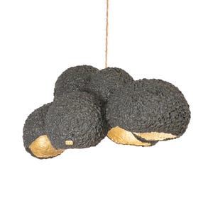 May include: A modern, black, textured pendant light fixture with four spherical shades. The interior of each shade is gold. The light hangs from a natural-colored rope against a white background.