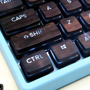 Pode incluir: Uma visão de perto de um teclado mecânico com caixa azul clara e teclas castanhas escuras. As teclas têm uma aparência de grão de madeira e letras brancas. O teclado inclui teclas com as etiquetas "TAB", "CAPS", "SHIFT" e "CTRL".