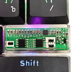 May include: Close-up of a computer keyboard with black keys. The "Enter" and "Shift" keys are visible, along with a circuit board. The circuit board is green with various electronic components.