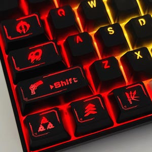 May include: A black mechanical keyboard with custom keycaps featuring red and yellow LED backlighting. The keys display various icons including a pistol, a knife, and the word Shift. The lighting creates a glowing effect between the keys.