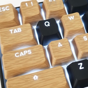 May include: Close-up of a mechanical keyboard with custom keycaps. The keycaps have a wood grain design with white lettering. Black keycaps are also present. The keyboard is lit from underneath, creating a bright glow.