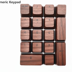 Könnte beinhalten: Ein numerischer Holz-Tastaturblock mit braunen Tasten. Die Tasten sind in einem Raster angeordnet und verfügen über Zahlen, Symbole und Funktionstasten. Der Text "Numeric Keypad" steht oben. Die Tasten haben eine Holzmaserung.