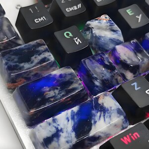 May include: Close-up of a computer keyboard with custom keycaps. The keycaps are made of a translucent material with a blue and white marbled pattern. Some keys have Cyrillic characters.