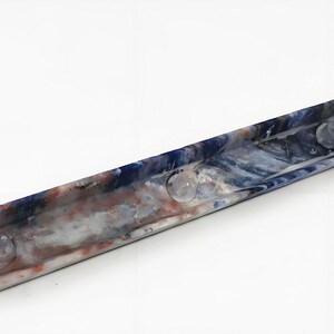 May include: A rectangular, marbled resin tray with a blue, white, and red color scheme. The tray has three clear, circular, raised accents. The tray is a decorative item.