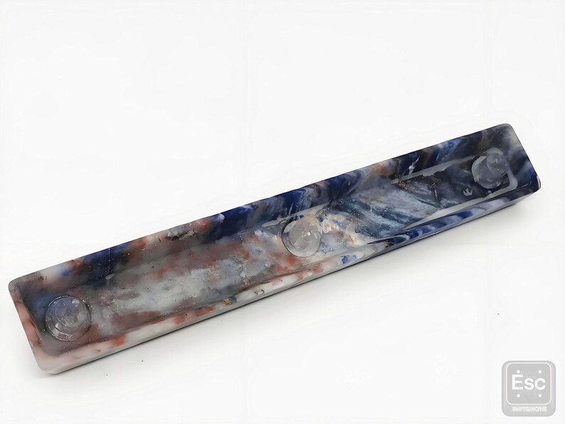 May include: A rectangular, marbled resin tray with a blue, white, and red color scheme. The tray has three clear, circular, raised accents. The tray is a decorative item.