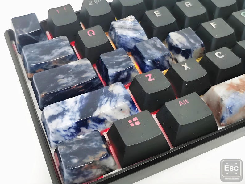 May include: Close-up of a mechanical keyboard with custom keycaps. The keycaps are made of a dark blue and white stone, with black keys in between. The keyboard has red LED lighting.