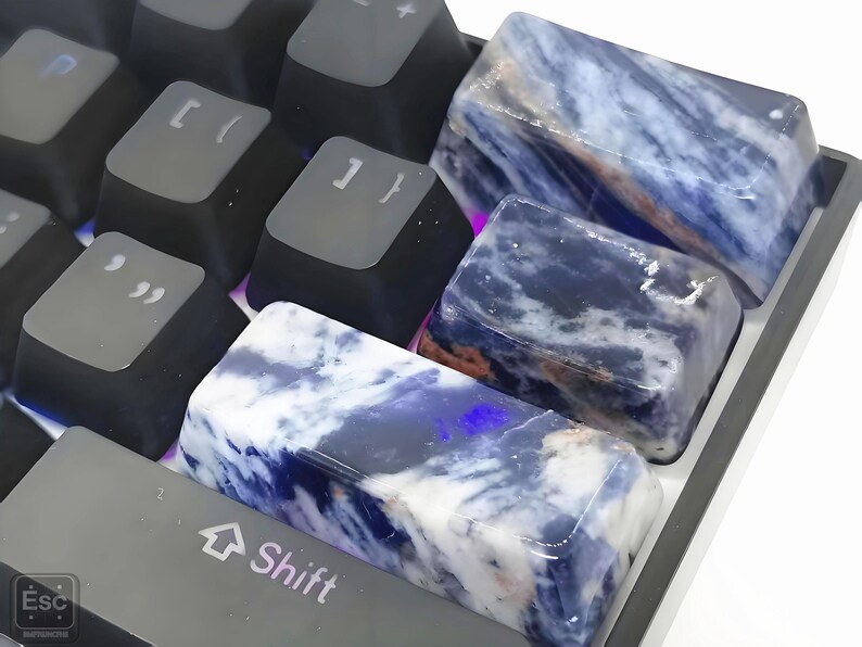 May include: Close-up of a keyboard with custom keycaps. The keycaps are made of a blue and white stone-like material. The keyboard keys are black and gray. The Shift key is visible, along with other keys.
